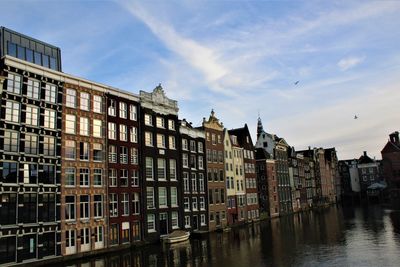 Buildings by canal against sky in city