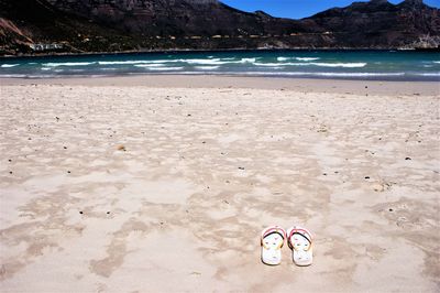 Shoes on sand at beach against sky