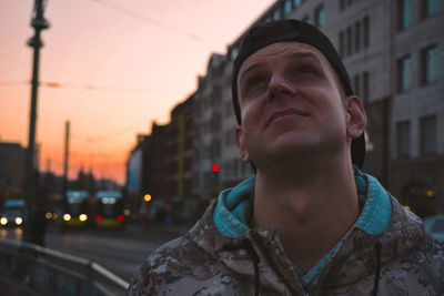 Portrait of young man in city against sky during sunset