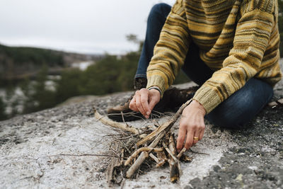 Low section of woman with sticks preparing campfire at mountain