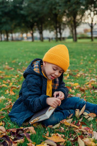 A little boy collects autumn leaves in a notebook.