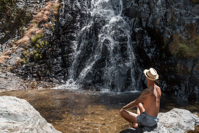 Rear view of shirtless man looking at waterfall