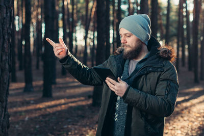 Young man standing by trees in forest