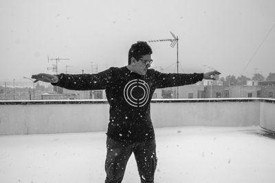 Front view of man with arms outstretched standing on building terrace during snowfall