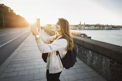 Side view of female tourist photographing through smart phone on bridge