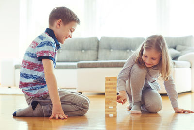 Full length of siblings playing with toy blocks on floor at home