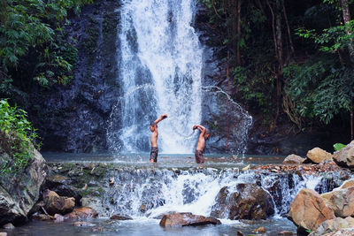 Side view of boys playing in river against waterfall