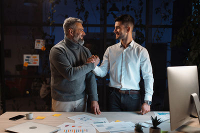 Male manager shaking hand to experienced senior colleague in evening office