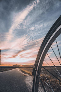 Road by railing against sky during sunset