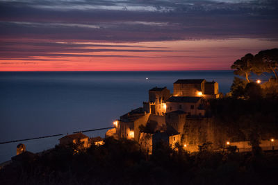 Illuminated historic village by sea against sky at sunset