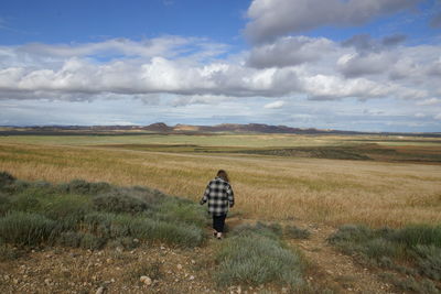 Rear view of woman walking on field against sky