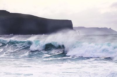 Waves splashing on shore against sky