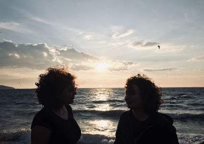 Friends on beach against sky during sunset