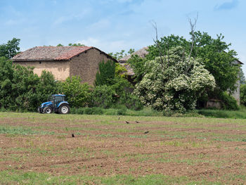 Blue tractor on a freshly plowed field with crows on it and farm nearby.