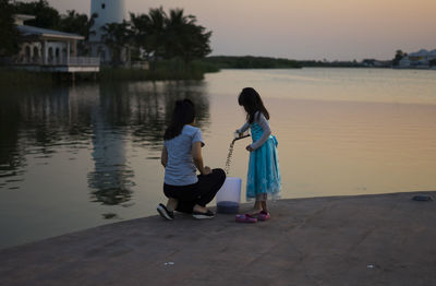 Full length rear view of women on shore against sky during sunset