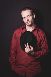 Portrait of mid adult man holding hat while standing against black background