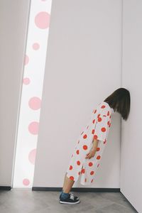 Rear view of woman standing against wall at home