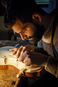 Male craftsman violin maker working on a new violin in the workshop