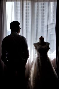 Rear view of man standing by window at home