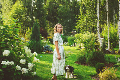 Portrait of smiling woman standing with dog against trees