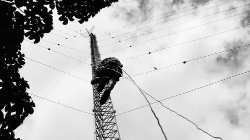 Rear view of man climbing communication tower against cloudy sky