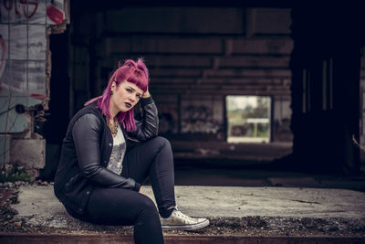 Portrait of young woman sitting by abandoned building