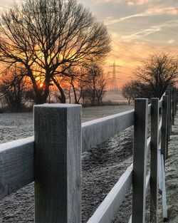 Bare tree in snow against sky during sunset