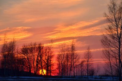 Silhouette bare trees by lake against romantic sky at sunset