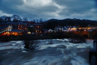 Town by river against cloudy sky