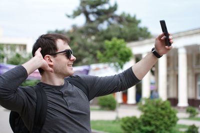 Smiling young man with hand in hair taking selfie on mobile phone in city