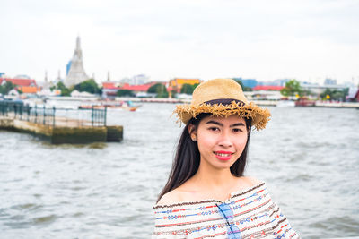 Portrait of smiling young woman standing against river