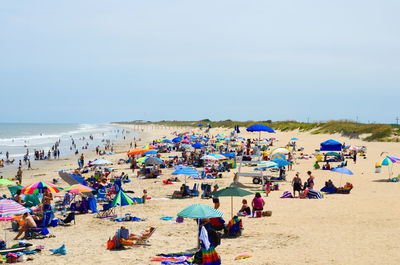 People with umbrellas at beach against sky on sunny day