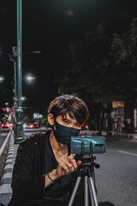 Portrait of man photographing on street in city at night