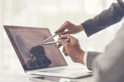 Midsection of businessmen pointing at laptop on table 