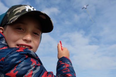 Low angle portrait of boy flying kite against sky
