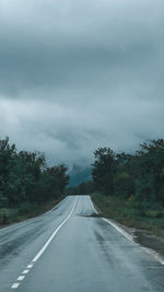 Empty road along trees and plants against sky