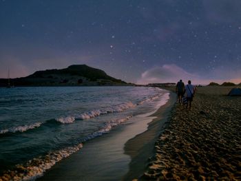 People walking at beach against sky at dusk