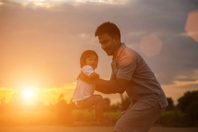 Rear view of mother and daughter against sky during sunset