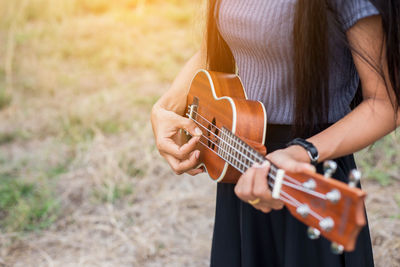 Midsection of woman playing guitar on field