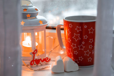 Winter still life with  mug with hot drink, two marshmallows, candle on window. valentine concept. 