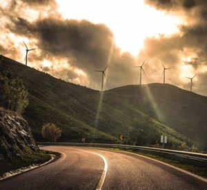 Road by wind turbines against sky