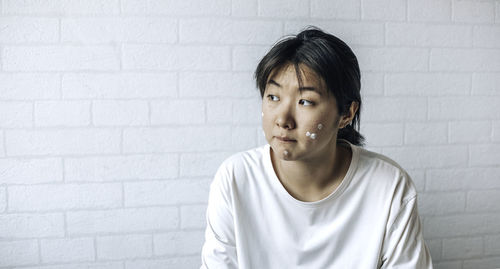 Teenage girl with problematic skin, with a therapeutic cream applied. white brick wall background