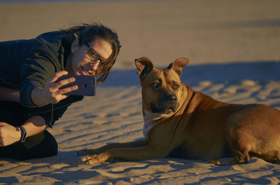 Young woman playing with dog at beach during sunset