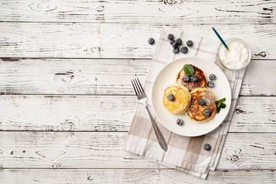 Cottage cheese pancakes served with curd and blueberries, top view flat lay on wooden background