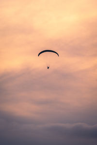 Low angle view of person paragliding against sky during sunset