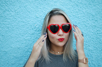 Young woman wearing heart shape sunglasses against blue wall