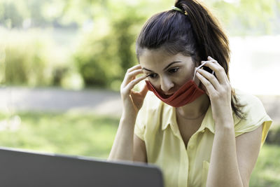 Woman wearing mask using laptop while sitting outdoors