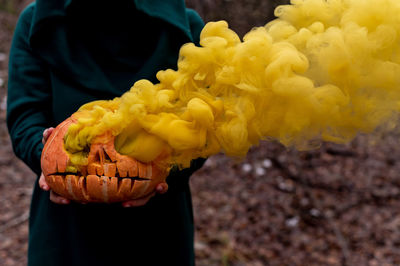 A creepy witch holds a steaming pumpkin in a deep forest. jack o lantern emits yellow smoke for