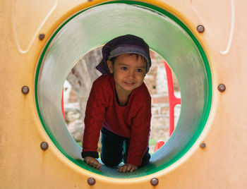 Full length of cute girl kneeling in outdoor play equipment in playground