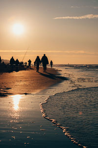 Silhouette people walking on beach against sky during sunset